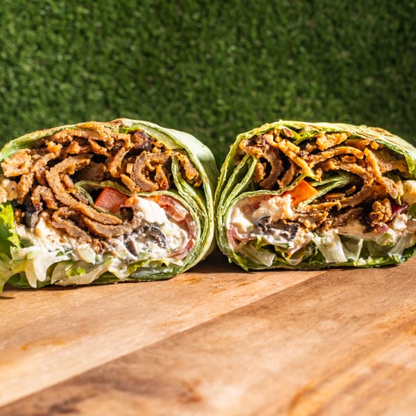 Two halves of a Wrap Happy wrap, filled with meat, lettuce, tomatoes, olives, and sauce.