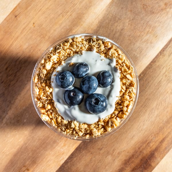 Overhead view of a yogurt parfait with granola, white yogurt, and blueberries on a wooden surface.