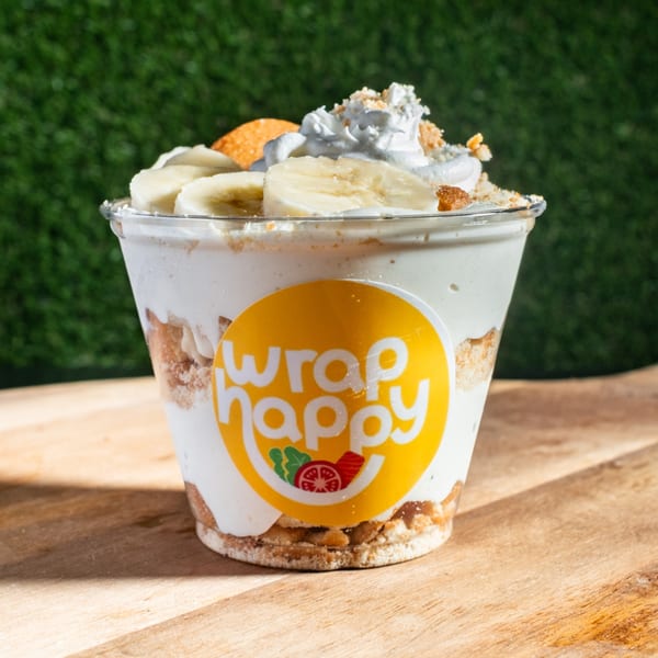A Wrap Happy banana pudding cup with whipped cream, banana slices, and cookie crumbles.