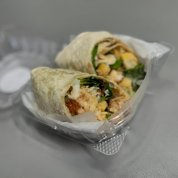 Two Wrap Happy wraps, filled with rice, chickpeas, and greens, in a clear plastic container.