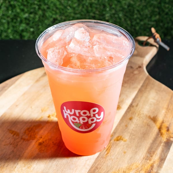 A Wrap Happy branded cup filled with a pink iced drink sits on a wooden board.
