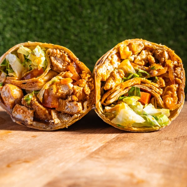 Two halves of a Wrap Happy chicken wrap, filled with meat, lettuce, and sauce, on a wooden board.