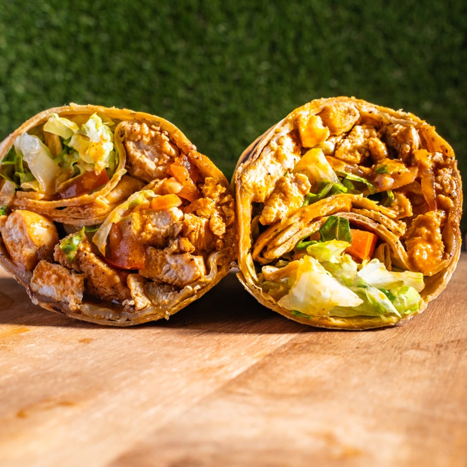 Two halves of a Wrap Happy chicken wrap, filled with meat, lettuce, and sauce, on a wooden board.