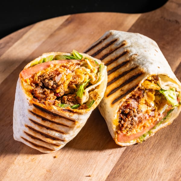Two grilled Wrap Happy wraps, cut in half, revealing seasoned meat, lettuce, and tomato on a wooden board.