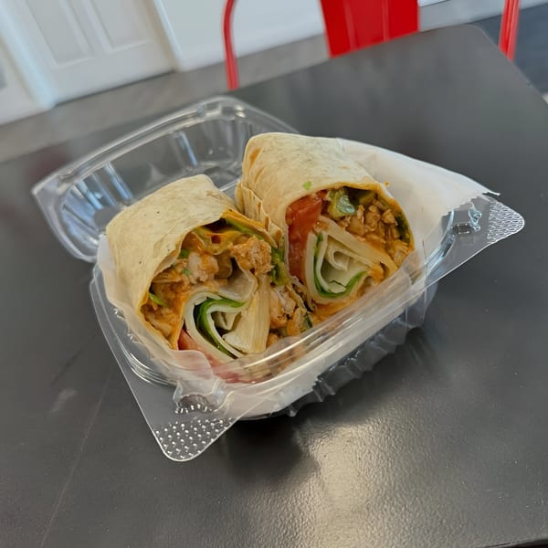 Two halves of a Wrap Happy wrap, filled with chicken, lettuce, tomato, and sauce, in a plastic container.