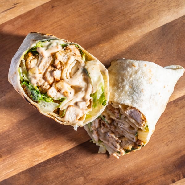Two halves of a chicken wrap, filled with meat, lettuce, and creamy sauce, on a wooden surface.